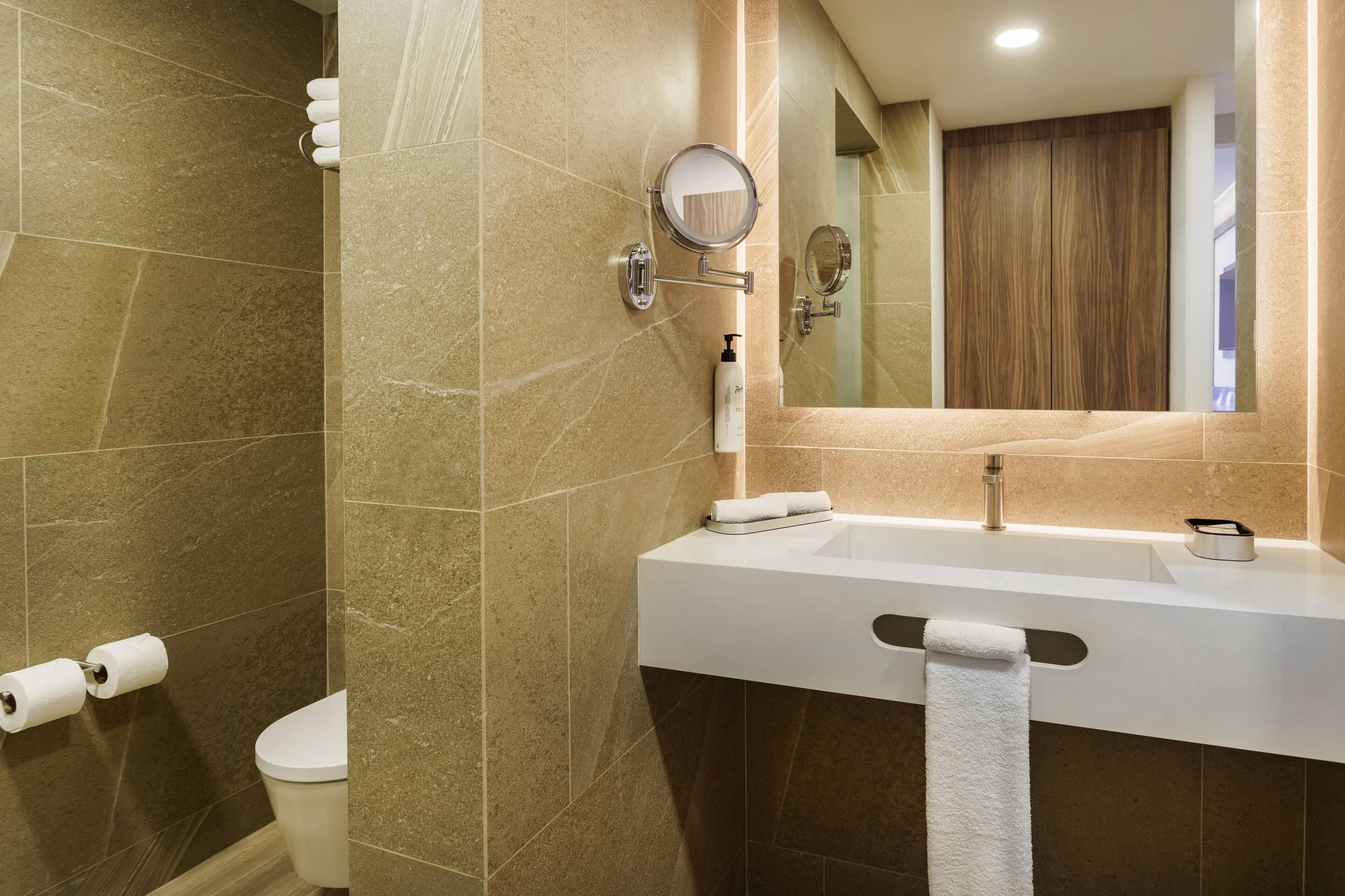 Un baño con inodoro, lavamanos con espejo y un perchero para toallas.