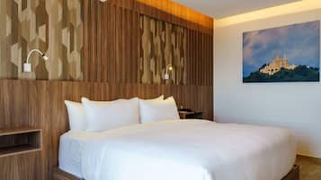 A hotel room with a wooden headboard, a bed with white linens, a nightstand, and a wall-mounted lamp.