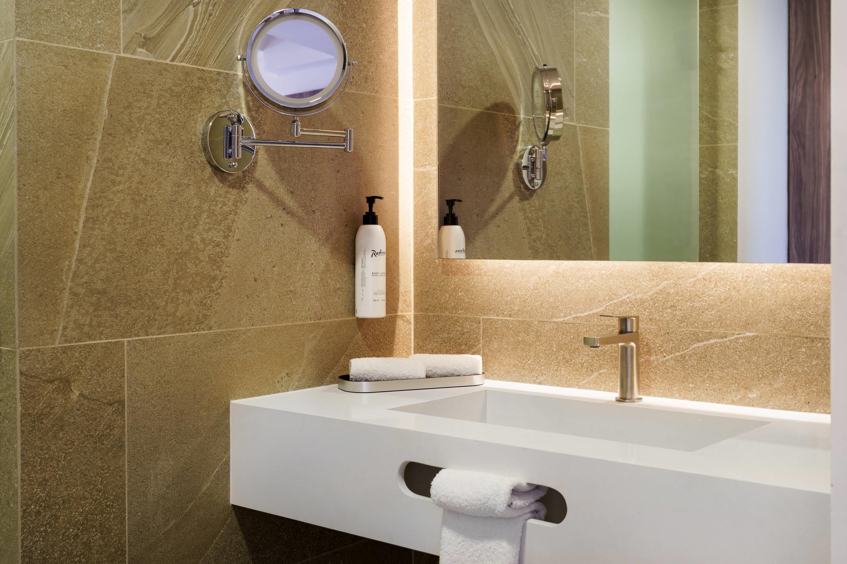 Un baño moderno con un lavabo blanco, un espejo, un perchero para toallas y una botella de champú.