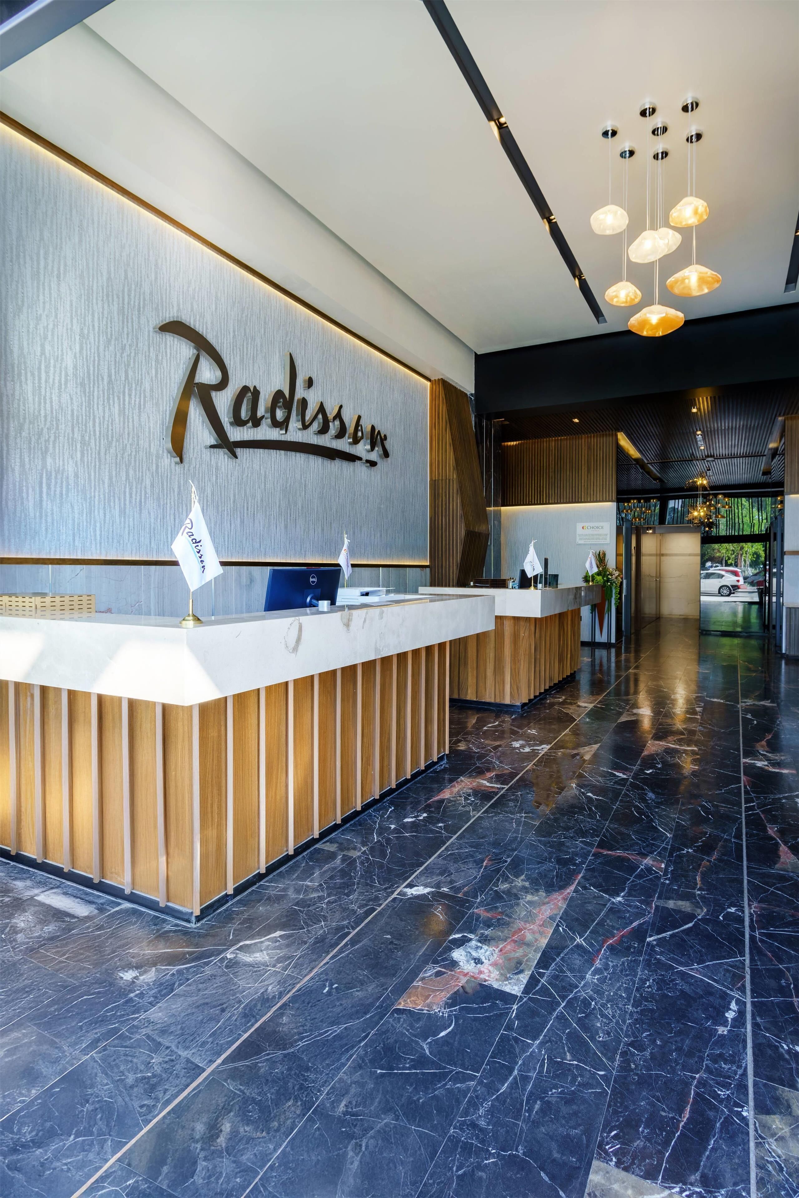 Un mostrador de recepción con un cartel que dice 'Radisson', un interior moderno con suelo de mármol y una araña.