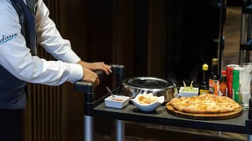 A person serving a pizza with various condiments and drinks on a tray.