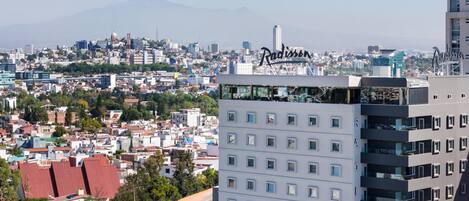 Un hotel moderno de gran altura, con varios balcones y vistas a la ciudad y una montaña al fondo.