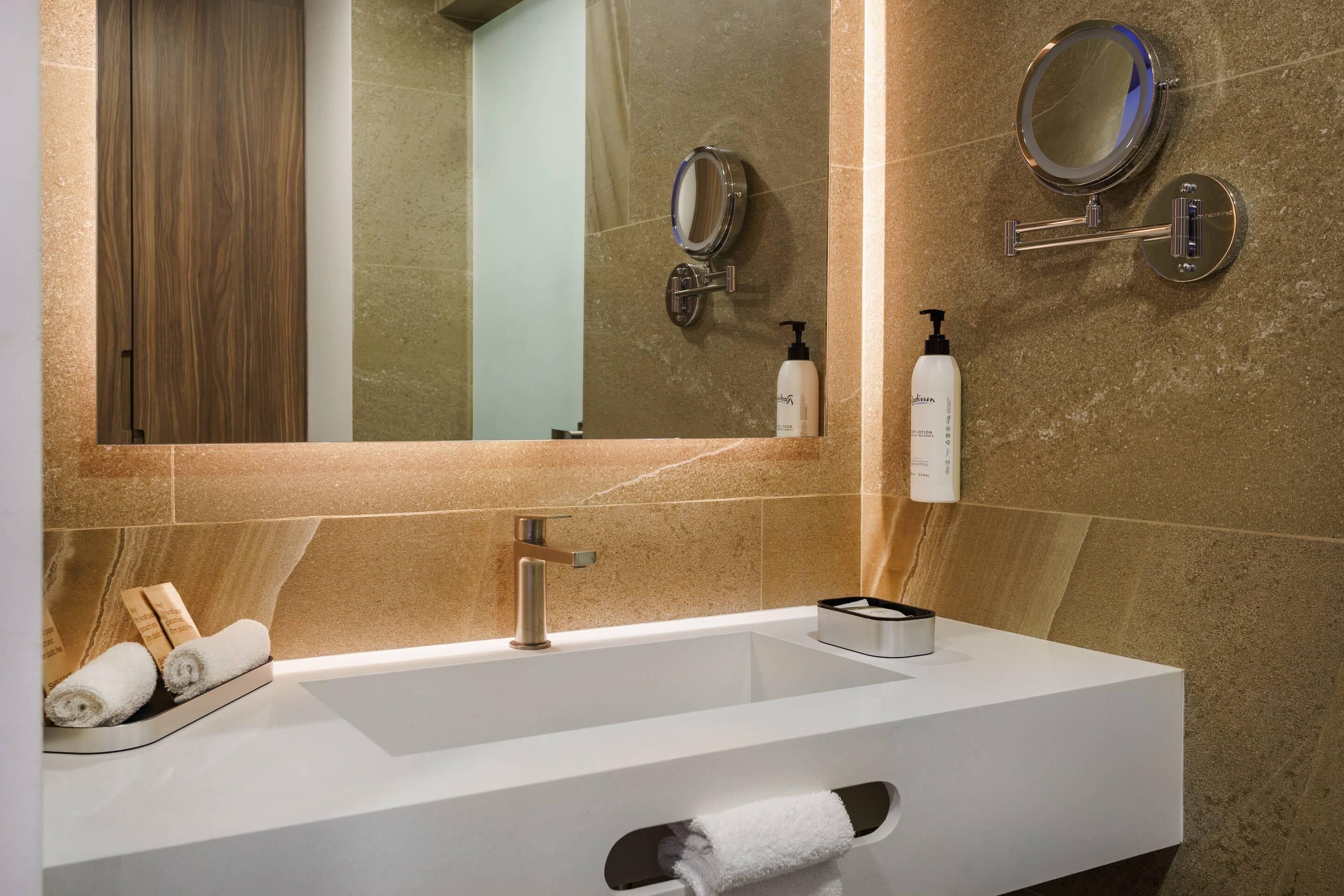 A modern bathroom with a large mirror, a sink, and a towel rack.