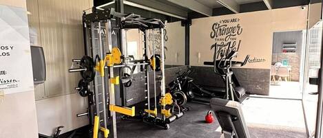 Un gimnasio con equipo de levantamiento de pesas, una cinta de correr y una frase motivacional en la pared.