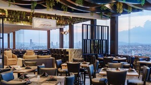 A restaurant with a city view, modern decor, and a mix of seating arrangements. - Radisson Puebla Angelopolis (Puebla)