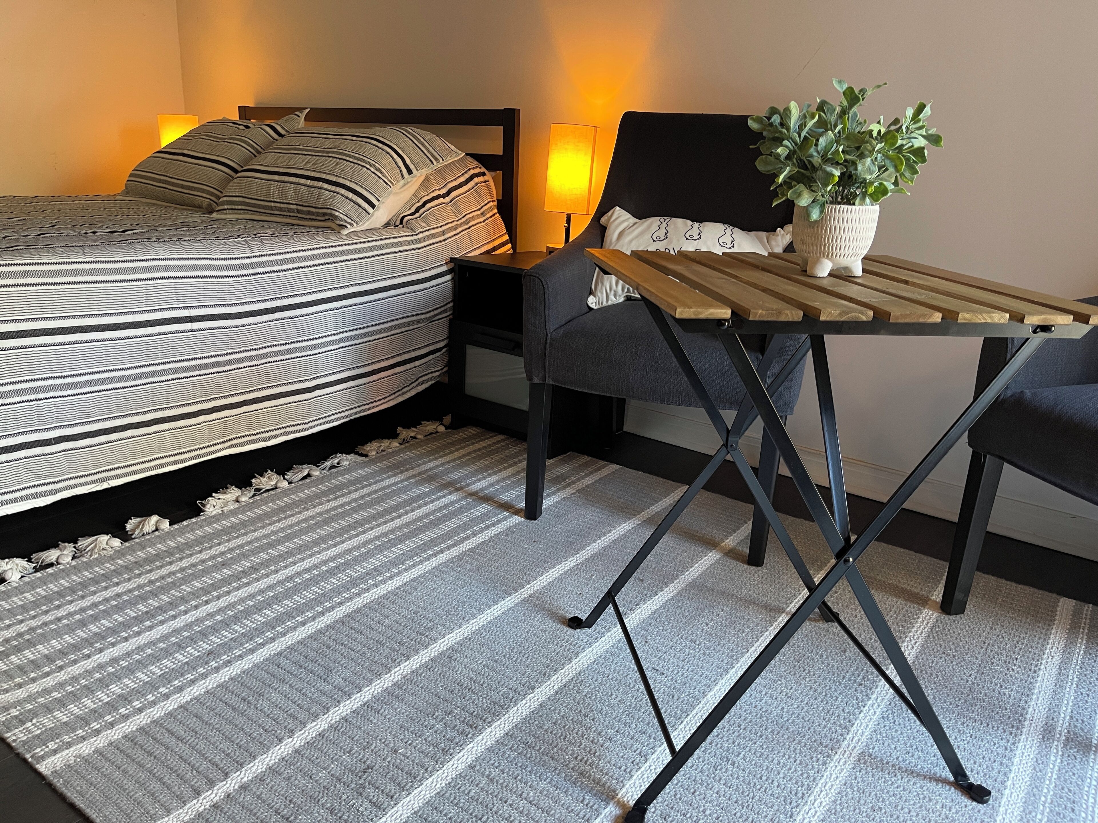 A neatly arranged bedroom with a bed, bedside tables, a small table, a chair, and a potted plant.