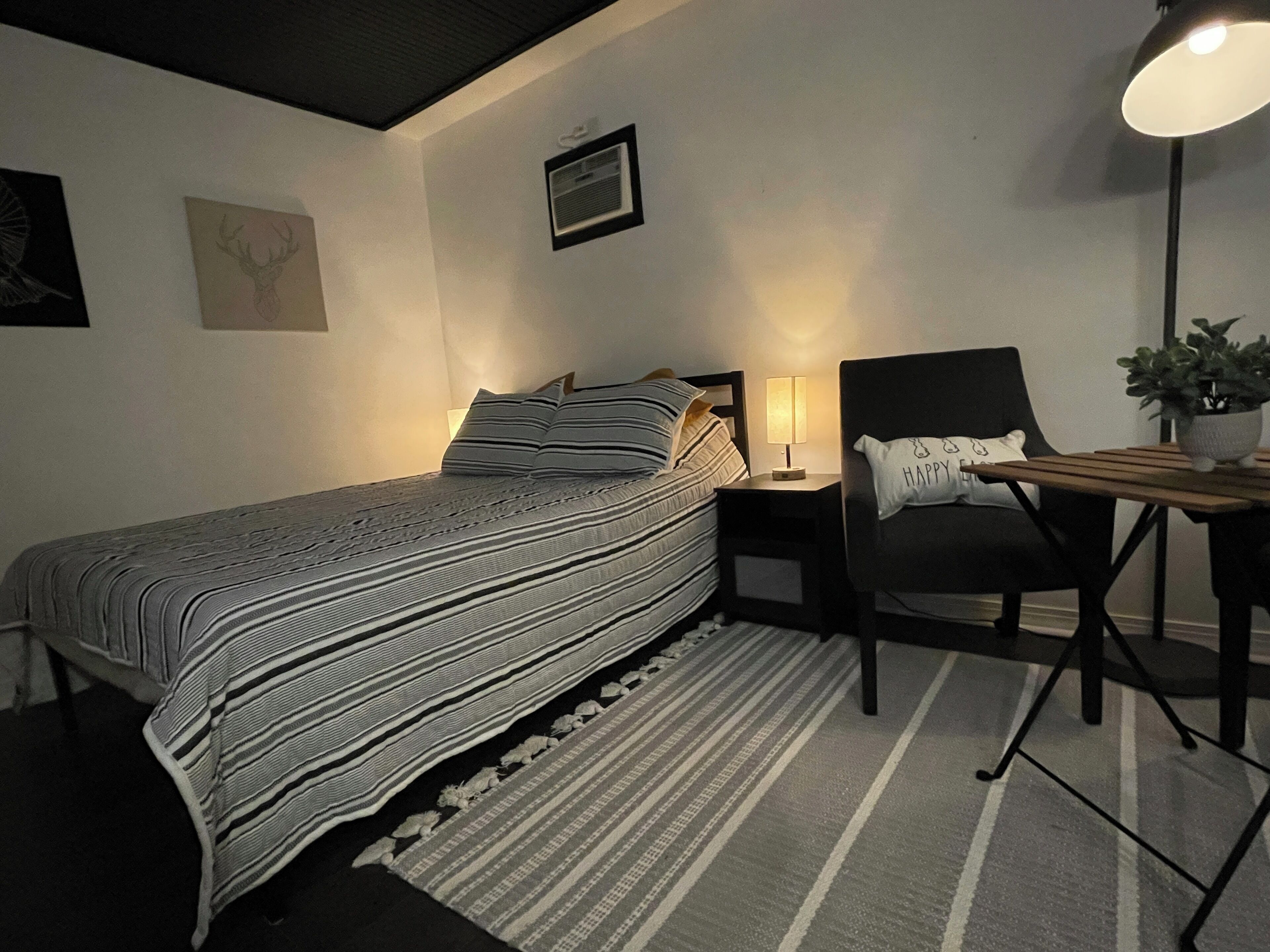 Un dormitorio ordenado con una cama, una silla, un escritorio y una lámpara.