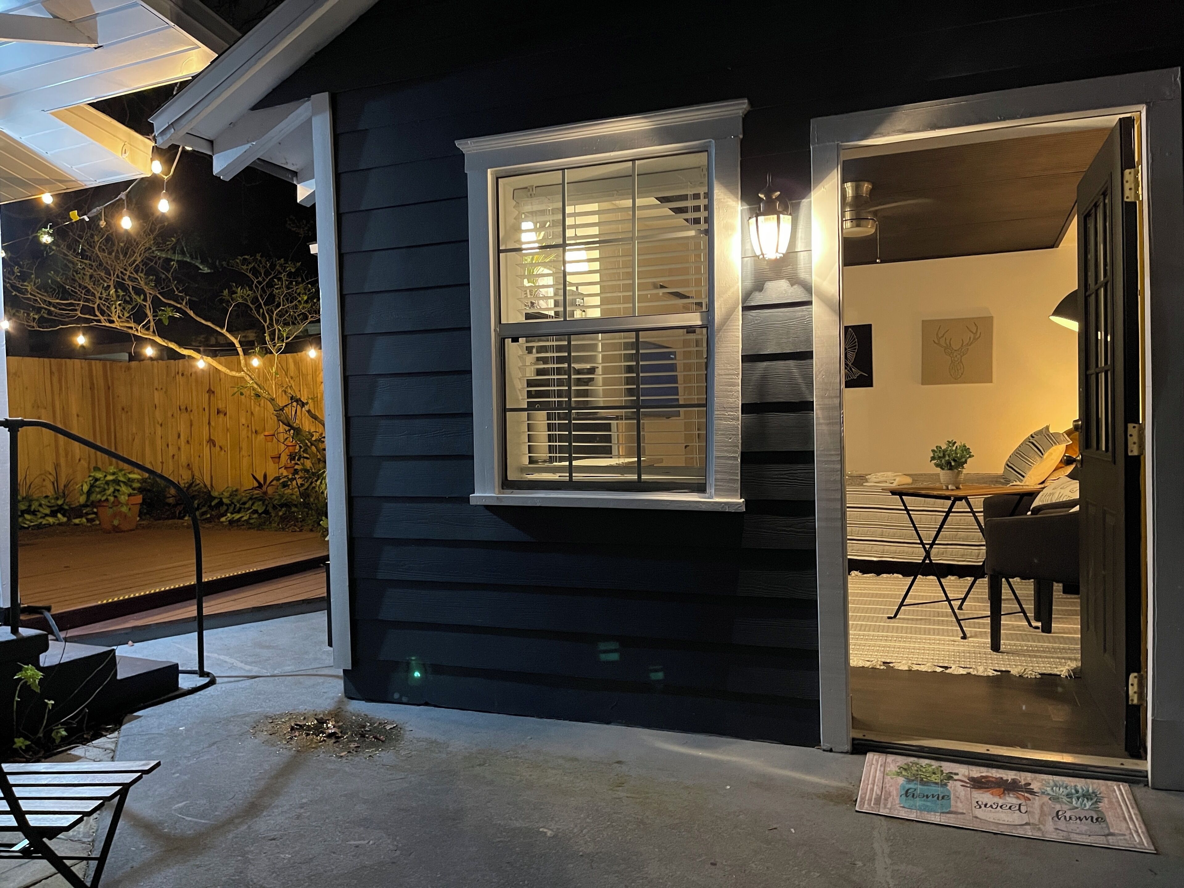 Uma casa de cor escura com janela aparente, porta de entrada e uma pequena área externa com banco e mesa.