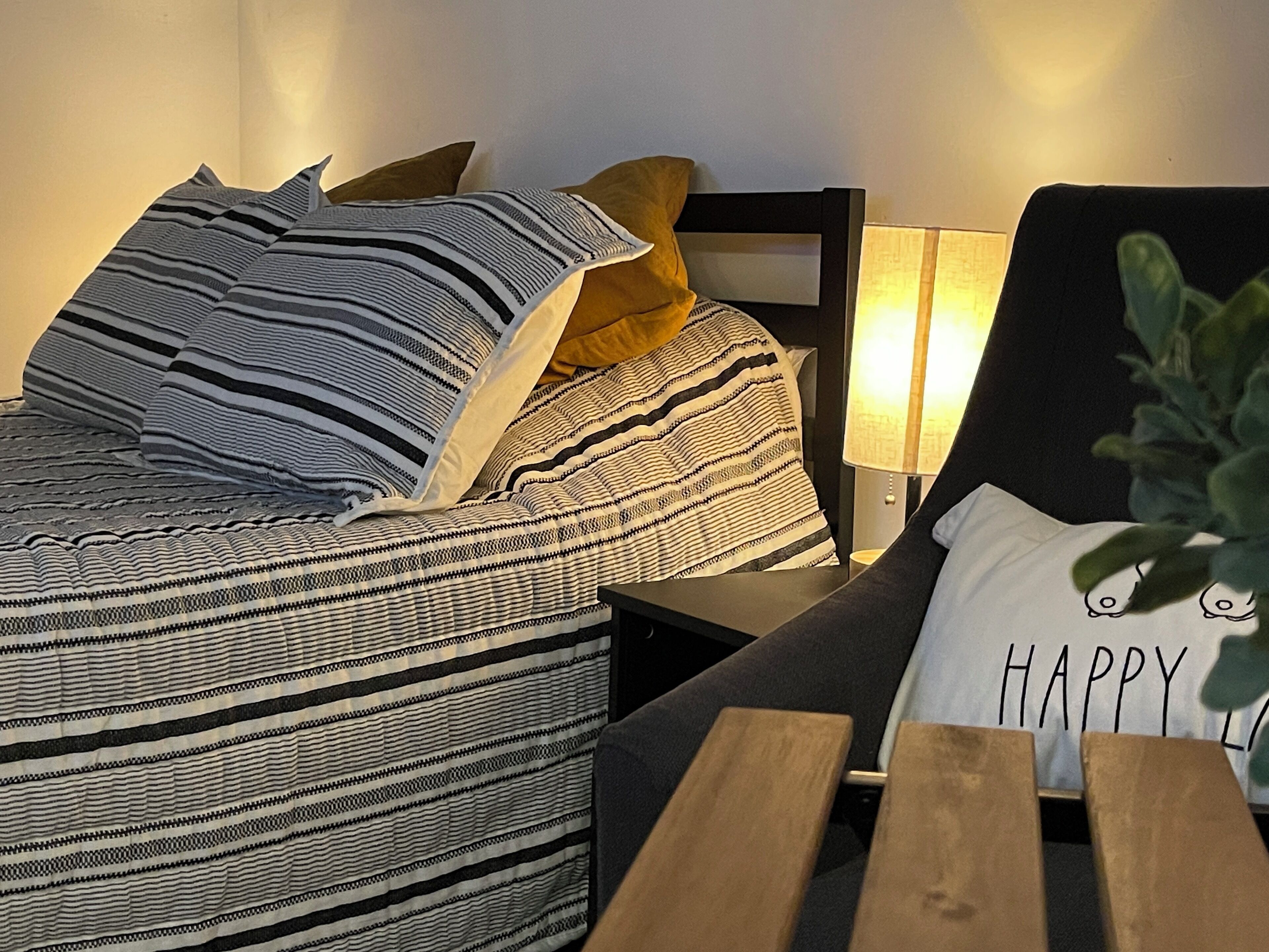 Een bed met streepjesbeddengoed, een nachtkastje en een nachtkastje met een lamp.
