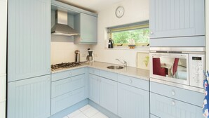 Una cocina con armarios azul claro, una estufa a gas, un lavamanos, un reloj y una ventana con vistas a la vegetación.