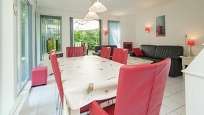 Amplia sala de estar con una mesa de comedor, sillas rojas, un sofá negro y un ventanal con vistas a la vegetación.