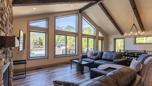 A spacious living room with a large sectional sofa, a fireplace, and large windows offering mountain views. - Ski In to your Private Hot Tub. Foosball Table. (Fernie)