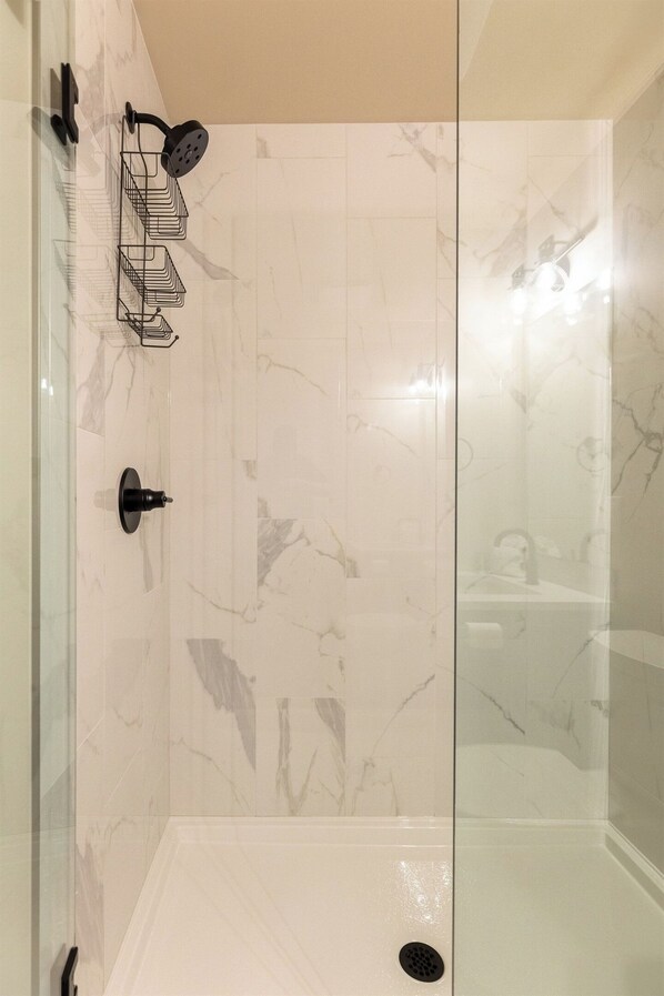 A glass-enclosed shower area with a marble wall, a black showerhead, and a black towel rack. - Ski In to your Private Hot Tub. Foosball Table. (Fernie)
