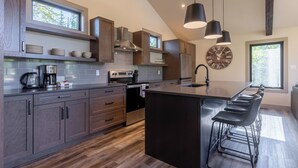 A modern kitchen with a large island, dark wood cabinets, and pendant lighting. - Ski In to your Private Hot Tub. Foosball Table. (Fernie)