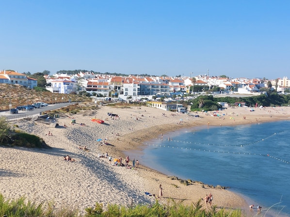 A beach with people, a road, and buildings in the background.