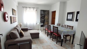 Un comedor con una mesa preparada para cuatro personas, un sofá y un cuadro grande en la pared.