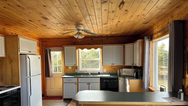 Cucina di una baita in legno con isola centrale, frigorifero, piano cottura e ventilatore a soffitto.