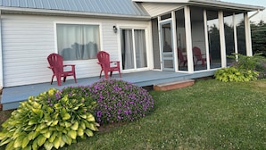 Una casa con un portico coperto, due poltrone Adirondack rosse e un giardino pieno di fiori viola.