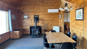 Accogliente interno di una baita con arredamento in legno, un tavolo centrale con sedie, un camino e una finestra che offre luce naturale.