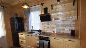 Una cocina tipo cabaña de madera con un refrigerador negro, armarios de madera, horno empotrado, un lavamanos y una lámpara colgante.