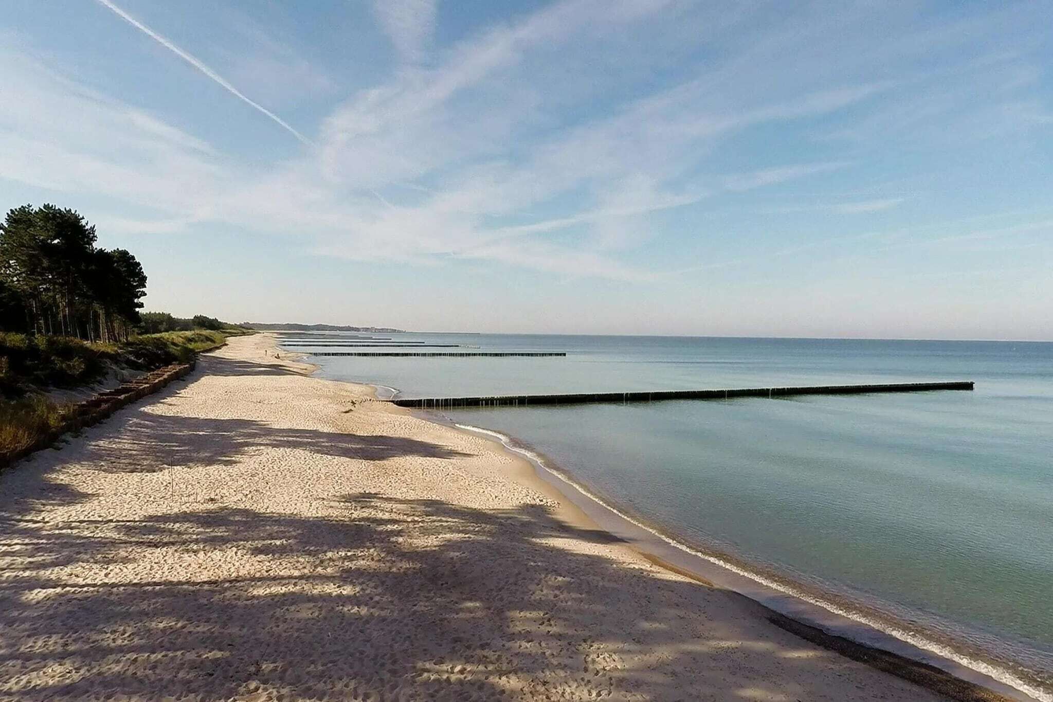 Une plage de sable fin, une eau calme, un ciel dégagé et une côte lointaine.