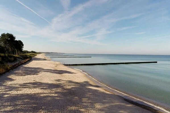 Una playa arenosa con aguas tranquilas, cielo despejado y una costa lejana.