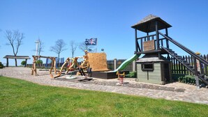 A playground with swings, a slide, and a small building with a roof.
