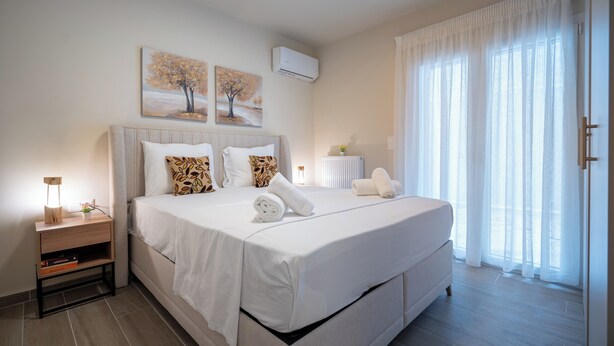 A modern bedroom with a large bed, a bedside table with a lamp, and two wall-mounted paintings. - Ilisia 2 person apartment by MPS (Athina)