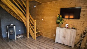 Un intérieur en bois avec un escalier en bois, une cheminée, un téléviseur fixé au mur et un meuble contenant des objets décoratifs.
