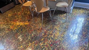 A dining area with a table and four chairs, a candle on the table, and a floor with a colorful abstract pattern.