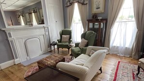 A traditional living room with a fireplace, a green armchair, a white sofa, and a patterned rug.