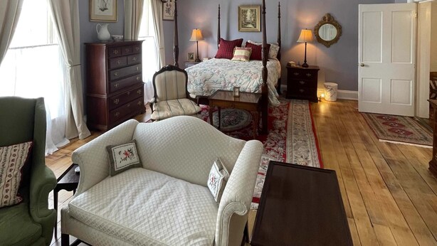 A room with a bed, a chair, a table, a ceiling fan, and a door.