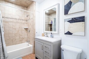 A bathroom with a bathtub, a toilet, a sink with a mirror, and two abstract paintings on the wall. - Fairfield Whole House (Fairfield)