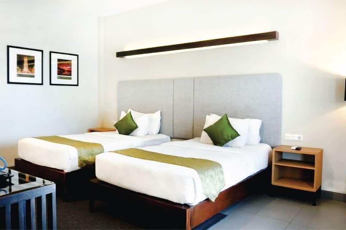 Une chambre d’hôtel avec deux lits, une table de chevet, un bureau et une étagère fixée au mur.
