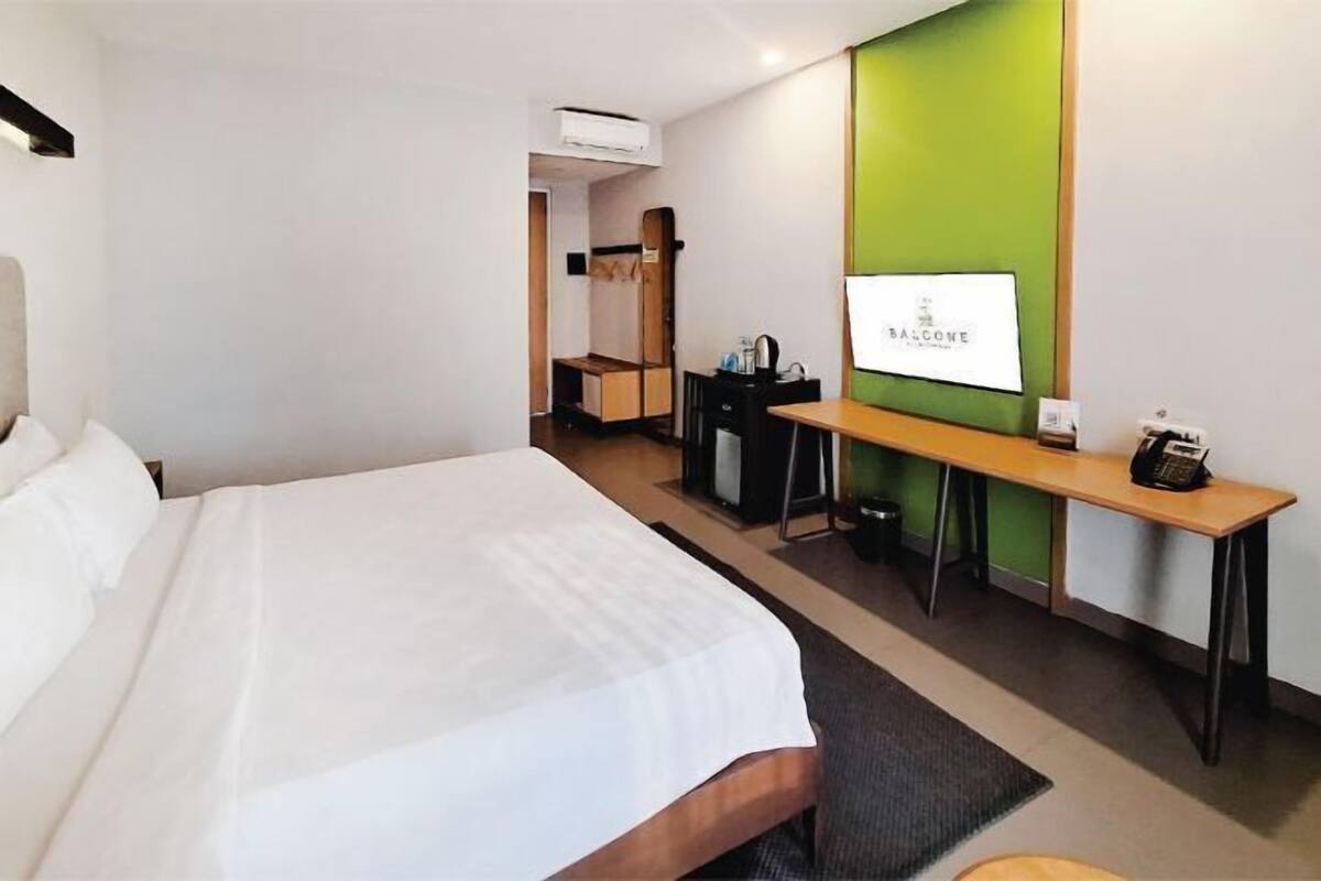 Une chambre d’hôtel avec un grand lit, un bureau avec un ordinateur, une chaise et une petite table avec un téléphone.