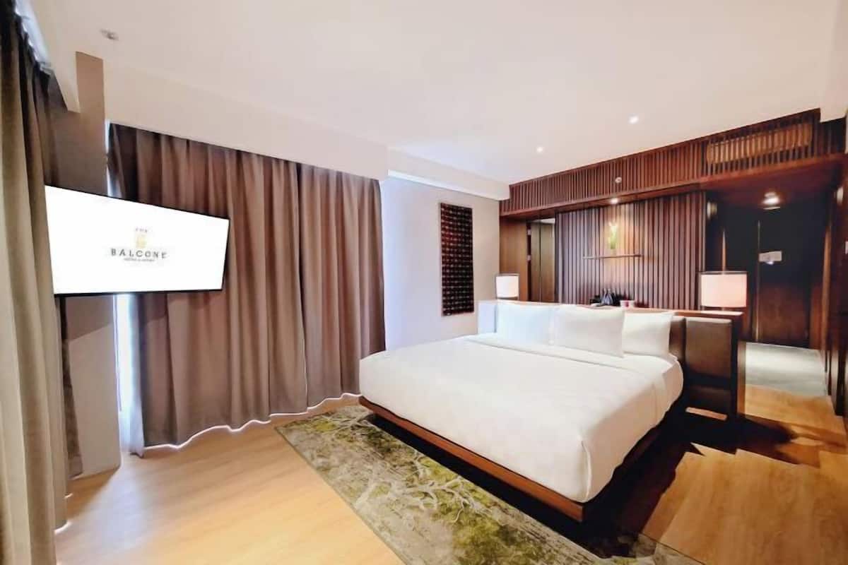 Une chambre d’hôtel moderne dotée d’un grand lit, d’un téléviseur à écran plat, de lambris en bois et d’un petit bureau avec une lampe.