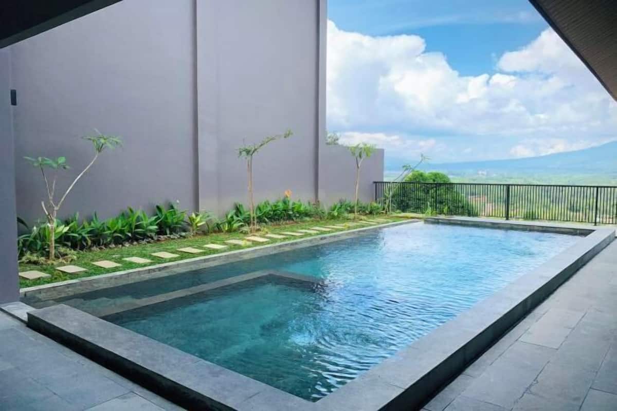 Une piscine rectangulaire à l’eau claire, entourée d’une terrasse en pierre et d’un petit muret de pierre.