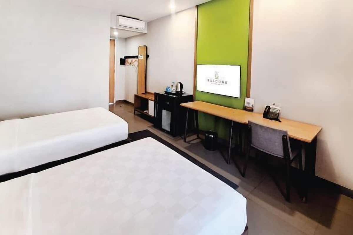 Une chambre d’hôtel avec deux lits, un bureau, une chaise, une petite table, un appareil de climatisation et un mur d’accent vert.