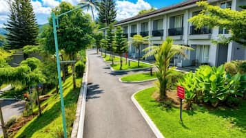 A pathway leading to a building with multiple balconies, surrounded by lush greenery and a clear sky.