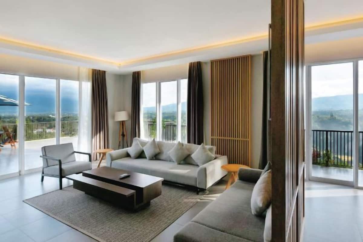 Un salon moderne avec un canapé, une table basse et un fauteuil, de grandes fenêtres offrant une belle vue et un balcon.