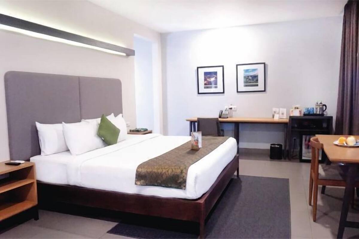 Une chambre d’hôtel comprenant un lit, une table de chevet, un bureau, une chaise et une petite table sur laquelle se trouve une assiette de fruits.