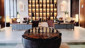 A modern lobby with a central seating area, a large water feature, and a wall of illuminated shelves. - The Balcone Suites & Resort (Gadut)
