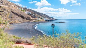 Un paysage côtier avec une plage, des collines rocheuses et un ciel bleu dégagé.