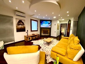 A living room with a sofa, a television, a fireplace, and a ceiling with recessed lighting.