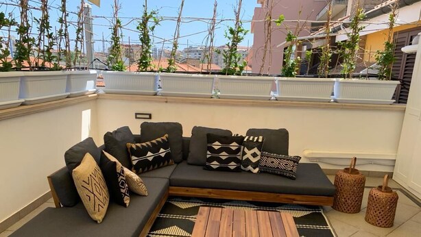 Una terraza en la azotea con un sofá modular, una mesa de centro de madera y una alfombra estampada.