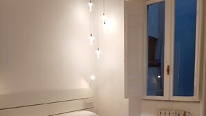 A modern bedroom with a large bed, a bedside table, a radiator, and a window with blinds. - Your Home In Trastevere (Roma)