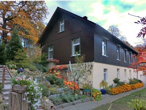Ein zweistöckiges Haus mit dunkelbrauner Fassade, einem Steinuntergrund und einem Garten mit verschiedenen Pflanzen und Blumen.