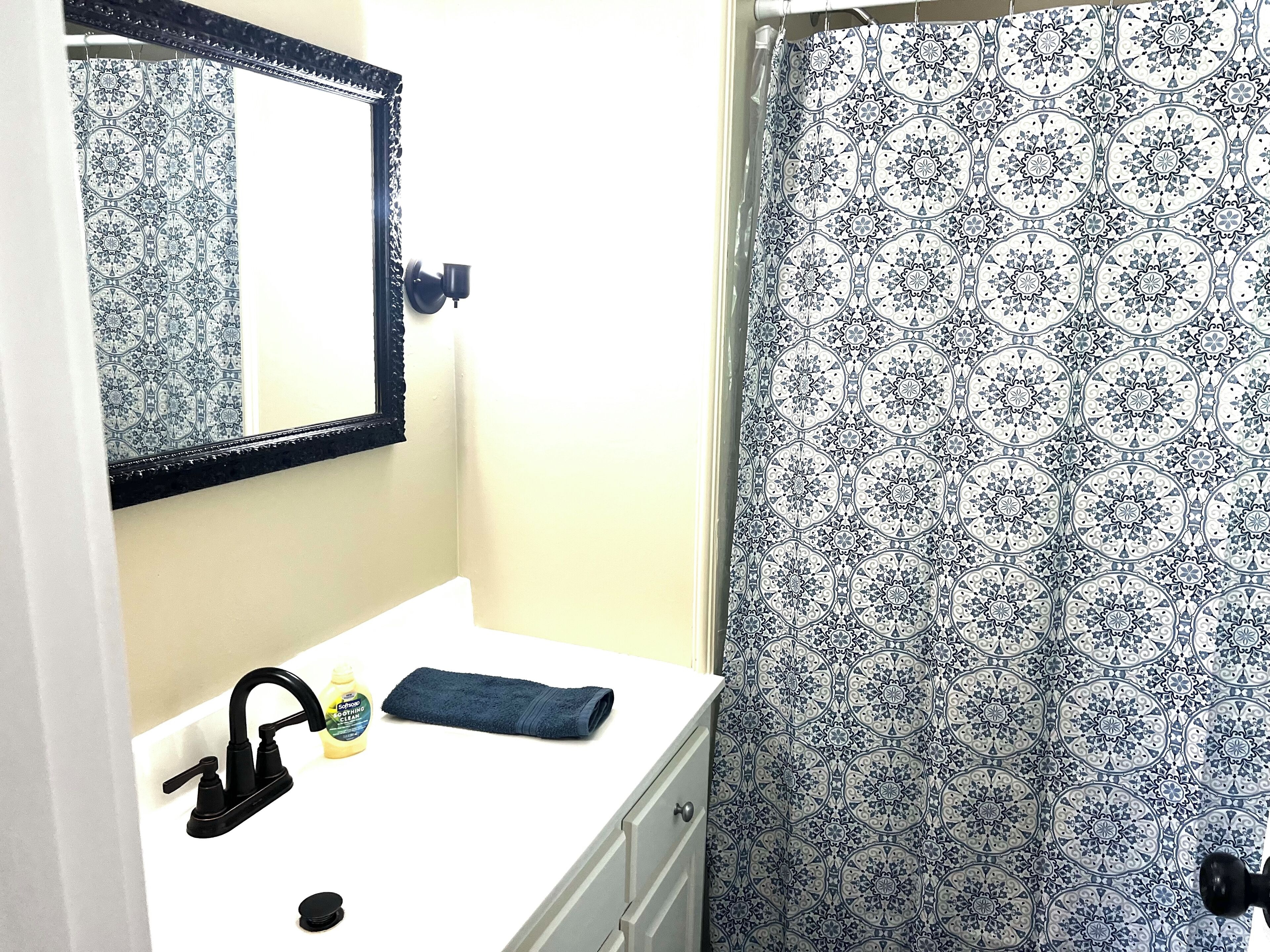 A bathroom with a white sink, black faucet, and a mirror with a black frame. There is a towel and a bottle of soap on the sink.