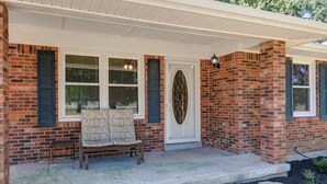 Une maison en briques avec un porche, un banc et une porte ornée d’un panneau de verre décoratif.