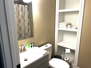 Une salle de bain équipée d’un lavabo, d’un miroir, de toilettes et d’étagères où sont rangées les serviettes.